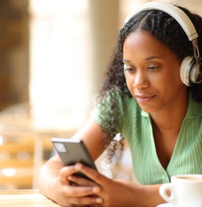 Black woman wearing headphone listening to music using phone and headphone in a bar terrace